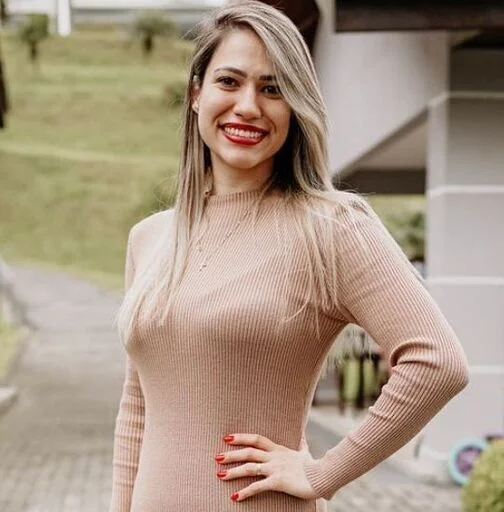 Portrait of Juliana Darwin Gonçalves smiling outdoors, in a ribbed beige dress, with greenery behind her