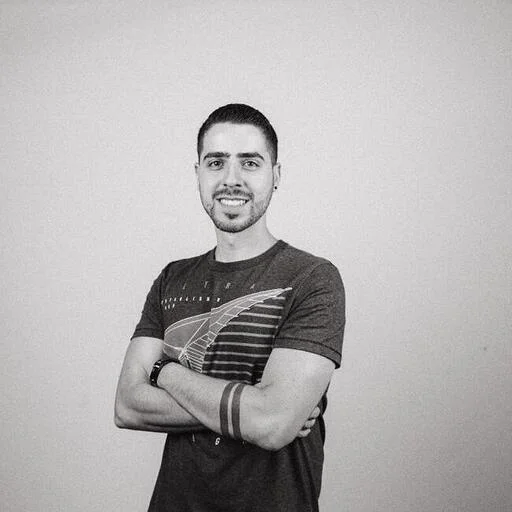 Black and white portrait of Marcelo Bavaroti with his arms crossed, in a dark t-shirt against a plain wall